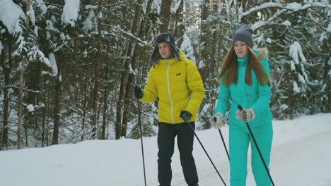 Smiling-girl-in-blue-jacket-skiing-rides-in-the-woods-with-her-boyfriend-in-winter-on-the-eve-of-Valentine's-day.-slow-motion.